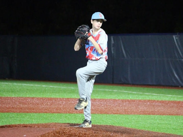 Noah Earhart mid-delivery on the mound during a night game, glove raised and front leg driven up